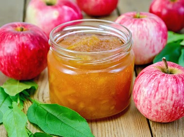Apple jam in a glass jar, fresh red apples, twigs with leaves on a wooden board